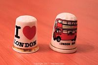 Photo of two porcelain London-themed collectible thimbles. One depicts a red London double-decker bus with 'Harrods London' and 'London Bus' text, the other says 'I Love London' with a red heart.