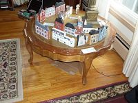 Wooden coffee table with glass top, holding multiple miniature decorative houses.