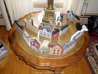 Overview of 26 hand painted wooden miniature houses arranged on a wooden table around a lamp base, showing various colors and styles.