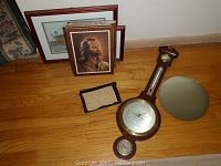Framed Memorial Stadium print, framed Jesus portrait, wooden wall barometer, and embroidered red car fabric piece on wood floor.