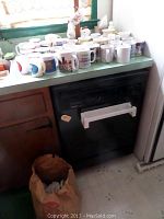 Photo of approximately 30 assorted used mugs arranged on a countertop, showing visible soiling and wear.