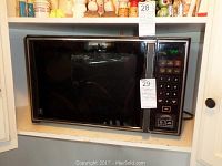 Front view of the black GE microwave oven installed in a shelf, showing keypad and door.