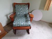 Wooden rocking chair with floral patterned cushions and a round glass table top placed beside it.