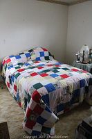 Full view of bed with colorful patchwork quilt covering it in a bedroom setting.