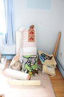 Photo of various pillows including a striped pillow and multiple colorful latch hook pillows featuring cartoon characters, plus rolled foam mats and folded textiles on the floor.