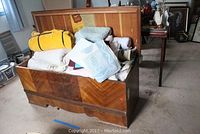 Overall view of open cedar chest filled with assorted linens and blankets inside a room.