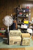 Four fans and heaters positioned together including one oscillating Duracraft pedestal fan, large box fan, smaller vintage box fan, and two electric radiant heaters (one boxed).