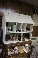 Full view of white wooden dollhouse with six sectional rooms on two shelves, each room containing various miniature furniture pieces.