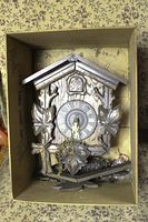 Overall boxed view of wooden cuckoo clock with detached wooden parts inside a box.