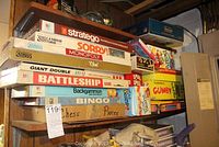 Photo showing stacked classic board games including Stratego, Sorry, Monopoly, Clue, Battleship, Backgammon, Bingo, Chess pieces, and Gumby game.