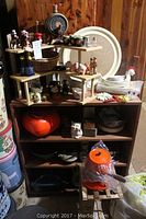 Overall view of kitchen shelf displaying orange fondue set, decorative keg, assorted salt and pepper shakers, ceramic figurines, and trays.