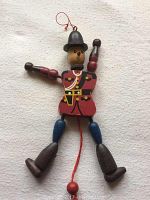 Full view of wooden RCMP marionette showing full body and limbs spread on a beige surface.