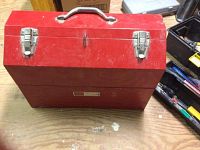 Red metal toolbox closed, shows surface wear and rust