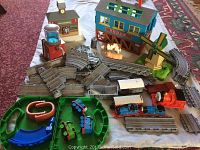 Overview of train set components with tracks, trains, and buildings arranged on cloth with visible animal figures and water tower accessory.