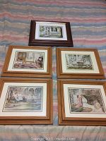 Five framed Trish Romance prints arranged on a bedspread, four with light wood frames and one dark wood frame, showing various romantic and domestic scenes.
