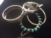 Photo showing three gold-toned bracelets: one with turquoise beads and broken safety chain, a textured bangle, and an enamel and rhinestone hinged bracelet.