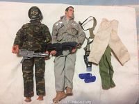 Two GI Joe dolls, one in camouflage with helmet and face paint, the other in gray jacket with patches. Accessories and extra pants laid out.