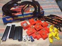 Photo showing black track sections, orange central crash mechanism with multiple rotary sections, yellow ramps, and three metal cars on display with original box underneath.