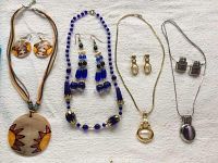 Four necklace and earring sets displayed on a white fabric background showing varying styles and colors.