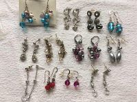 Full view of twelve pairs of earrings arranged on a cloth background showing a variety of styles, beads, and metallic finishes.