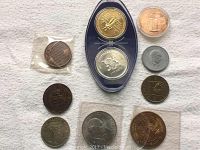 Lot of 11 commemorative coins in various conditions displayed on a flat surface including coins in plastic sleeves and a small display case with two coins.