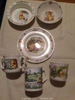 Overview photo showing all 6 pieces of the set laid out including 2 plates, 1 bowl, and 3 mugs all decorated with Winnie the Pooh scenes.
