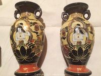 Front view of two matching Asian vases, showing detailed raised faces and lotus flower artwork on yellow and black background