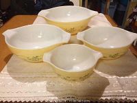 Four yellow Pyrex bowls with green floral design showing nesting set, each with handles and spouts, white interior
