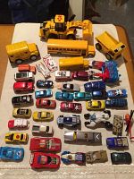 Top-down view of about 40 toy vehicles arranged on a surface, including cars, buses, construction vehicles, and a military tank.
