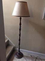 Full view of tall wood floor lamp showing turned wood base and beige fabric shade.