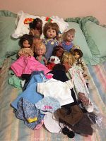 Wide view of assorted dolls and doll clothes including Holly Hobbie and Tickle Toes dolls on a couch