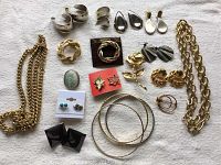 Assorted jewelry laid flat on a light-colored cloth background, showing all items in the lot including necklaces, multiple styles of earrings, brooches, and bangles.