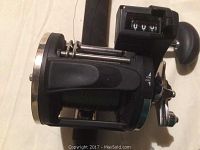 Side profile of the black baitcasting reel showing spool, handle, and attached line counter with an on/off switch seen on the side.