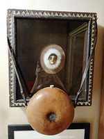 Front view of shadow box frame with sculpted face surrounded by white fur and attached primitive gourd canteen.