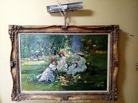 Full view of impressionist style painting depicting outdoor garden scene with figures, set in an ornate gilt frame with attached light above.