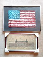 Photo showing both framed pieces: American flag textile art above and Ellis Island map below, with protective corners on the map frame.