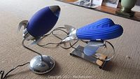 Two blue glass and metal lamps in shapes of rocket and airplane on beige carpet.