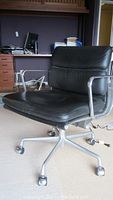 Front view of black leather office chair showing seat, back cushions and metal armrests