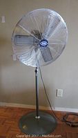Full view of Global heavy duty industrial floor fan showing tall stand, round base, five metal blades, and cord.