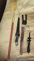Long pole weapon with brass blade, two daggers with sheaths and multiple leather accessories arranged on fabric background