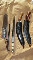 Five items laid out: dagger with brown leather sheath, telescopic baton and sheath, two kukri scabbards