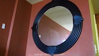 Front view of large round mirror with black ridged frame and beveled glass reflective surface.
