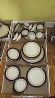 Three open cardboard boxes showing grouped plates and cups in Regency pattern