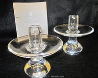 Pair of Steuben glass candlesticks shown with care instruction booklet, on black fabric background.