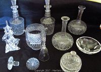 Group photo showing multiple cut-glass crystal items including three decanters, ice bucket, vases, glass bell, and glass Christmas tree sculpture on black background.