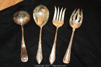 Four utensils laid side by side: two ladles (small and large) and two four-tine forks (plain and pierced) on black background