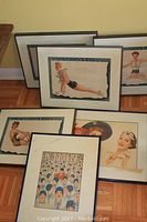 Six framed prints arranged on floor against wall, showing partial views of vintage style pin-up illustrations and crowd scene print labeled 'JUDGE'.