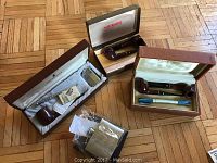 Three open Kaywoodie boxes showing multiple pipes and accessories on wood floor