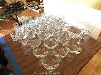 Various clear stemware glasses arranged on a table, including wine glasses and cocktail glasses, with a large bowl and pitcher visible in the background.