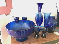 Photo showing the overall set of cobalt blue glassware including footed bowl, tall vase, two stemmed glasses, cobalt jar, and silver decorated shots.